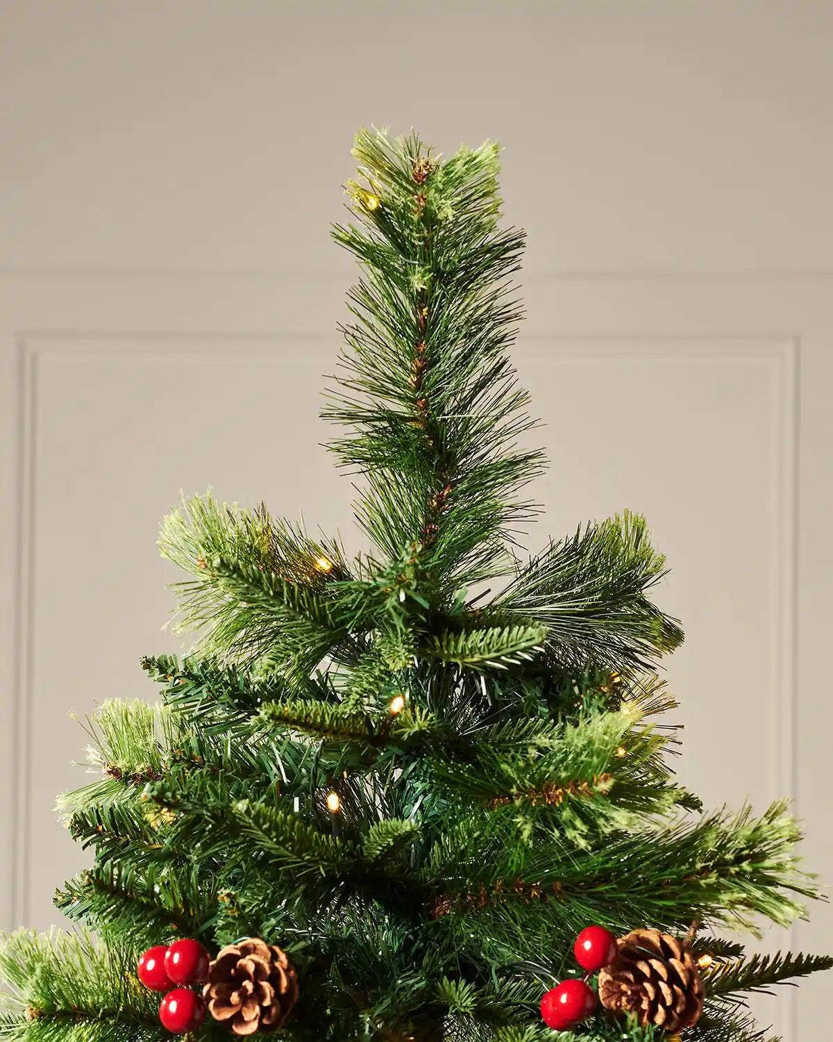 Top section of pre-lit Victorian Christmas tree with mixed green foliage, berries, pinecones and warm white lights