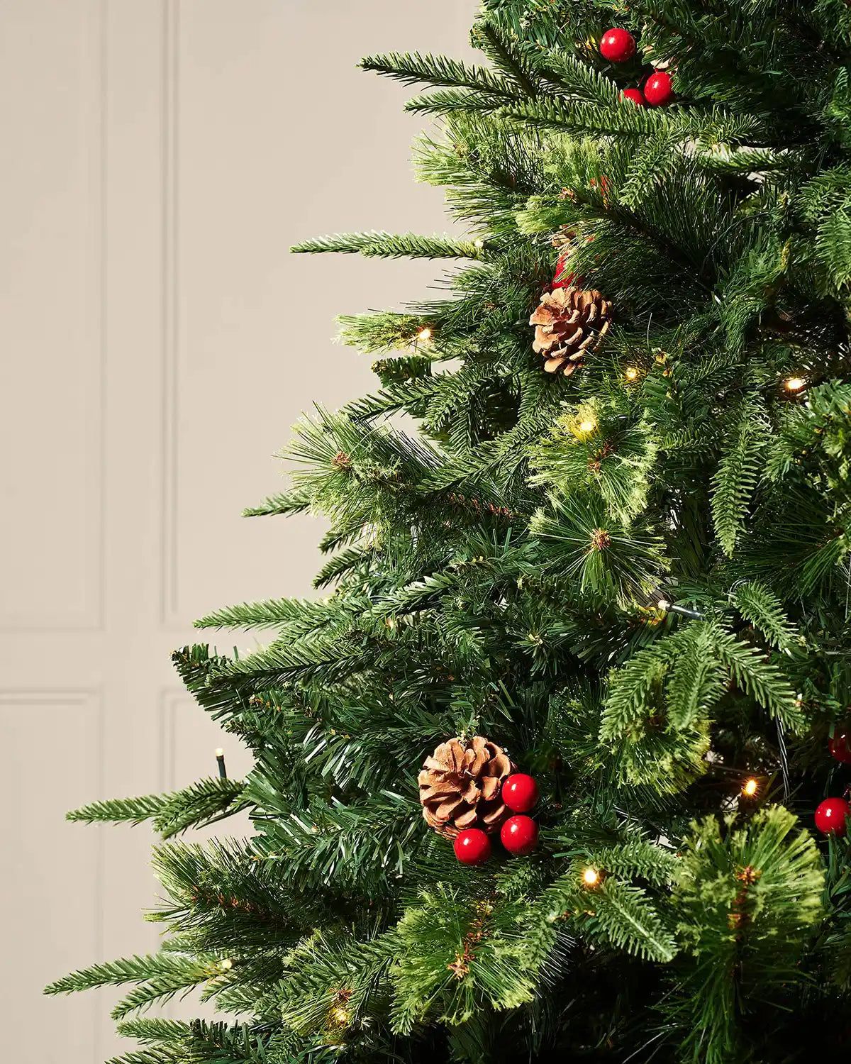 Close-up of mixed PE and PVC Christmas tree branches with pinecones, red berries and warm white LEDs