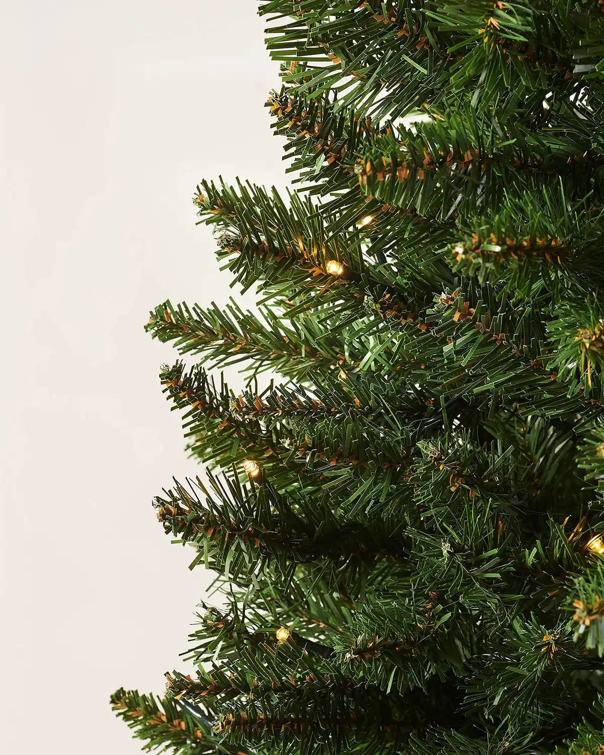 Close-up of green branches and warm white LED lights on the wall mounted Christmas tree