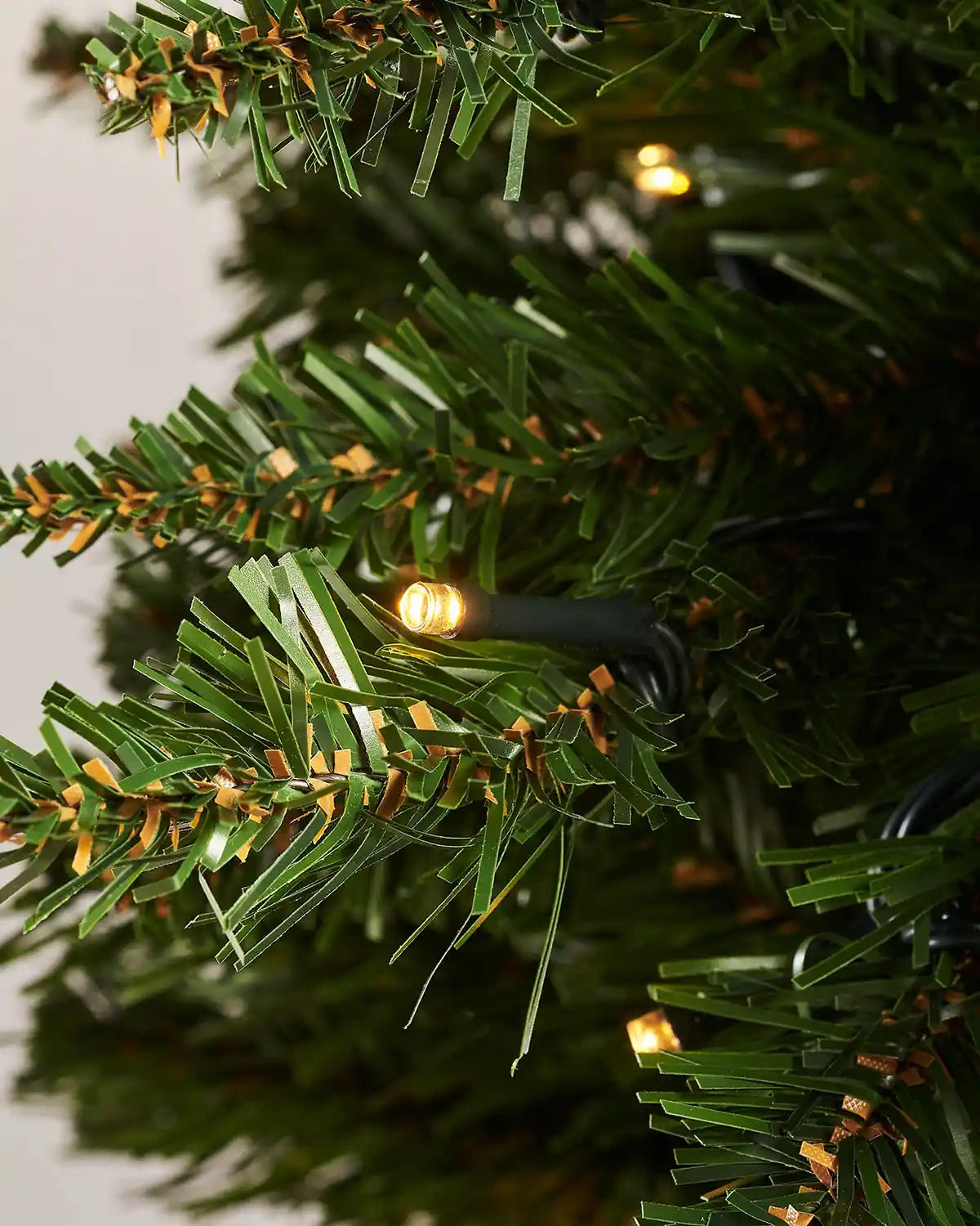 Close-up of a warm white LED bulb among the green branches of the wall mounted tree