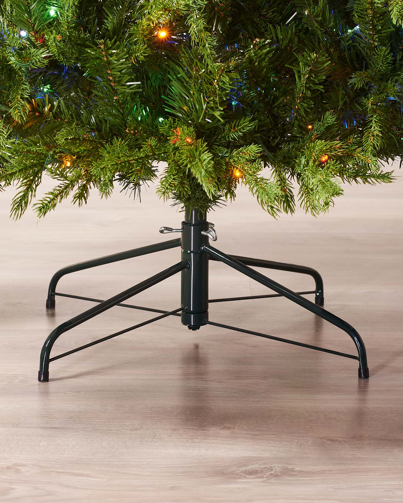 Close-up of the lower branches and black metal tree stand on a wooden floor.