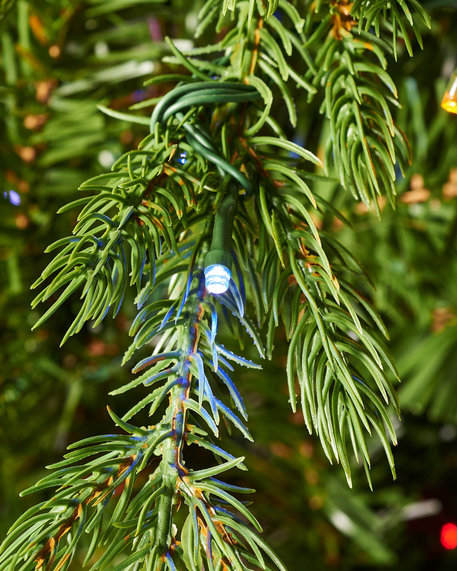 Close-up of warm white LED lights nestled among realistic green fir branches.