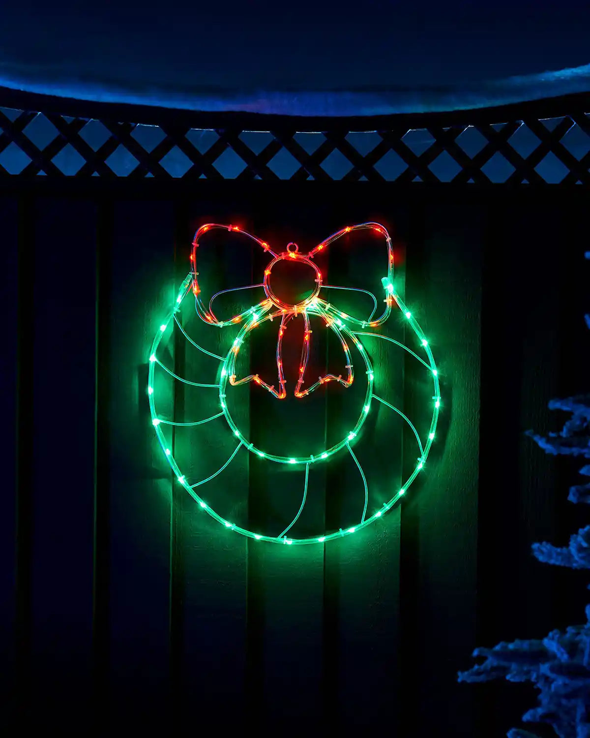 Pre-lit wreath and bow rope light displayed on a wooden wall at night