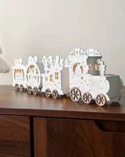 Full image of pre-lit white wooden train decoration on dark wood surface in front of white wall