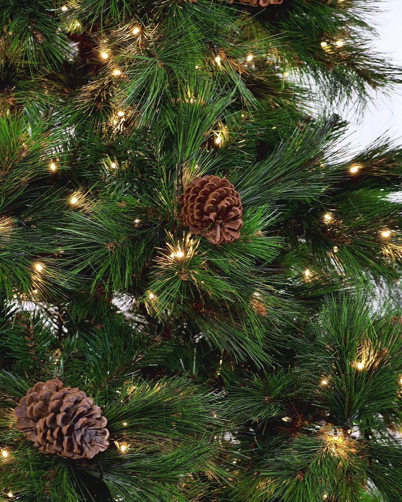 A 7-foot pre-lit Portland spruce Christmas tree with pinecones and warm white LED lights, placed in a living room with neutral décor.