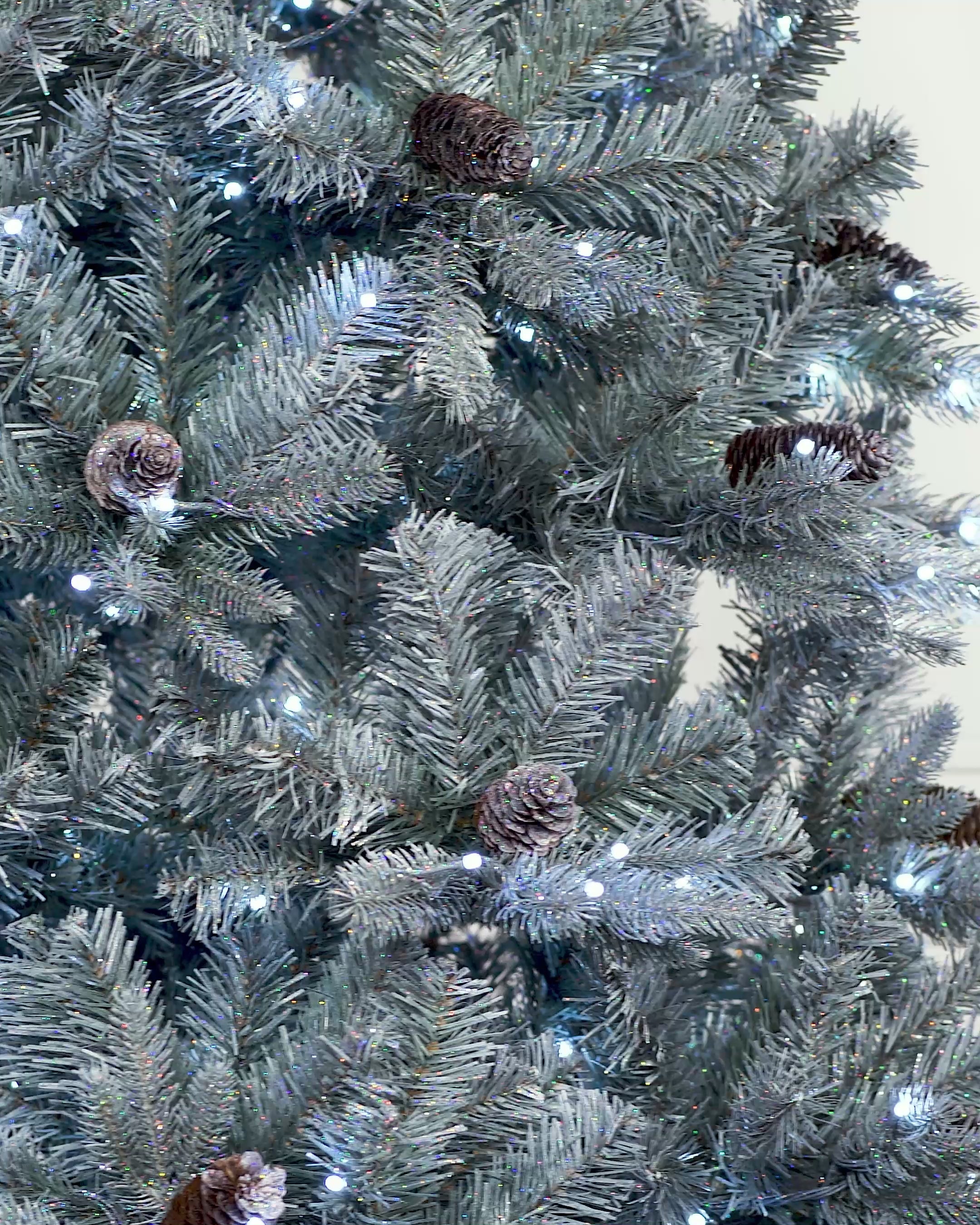 Load video: Pre-lit Elegant Spruce artificial Christmas tree with mixed PE and PVC branches, realistic pinecones, glitter finish, and bright white LED lights with multi-function settings, displayed in an indoor setting.