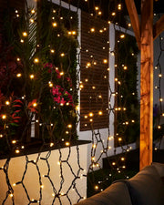 Close-up of warm white curtain lights on black cable hanging in an outdoor seating area.