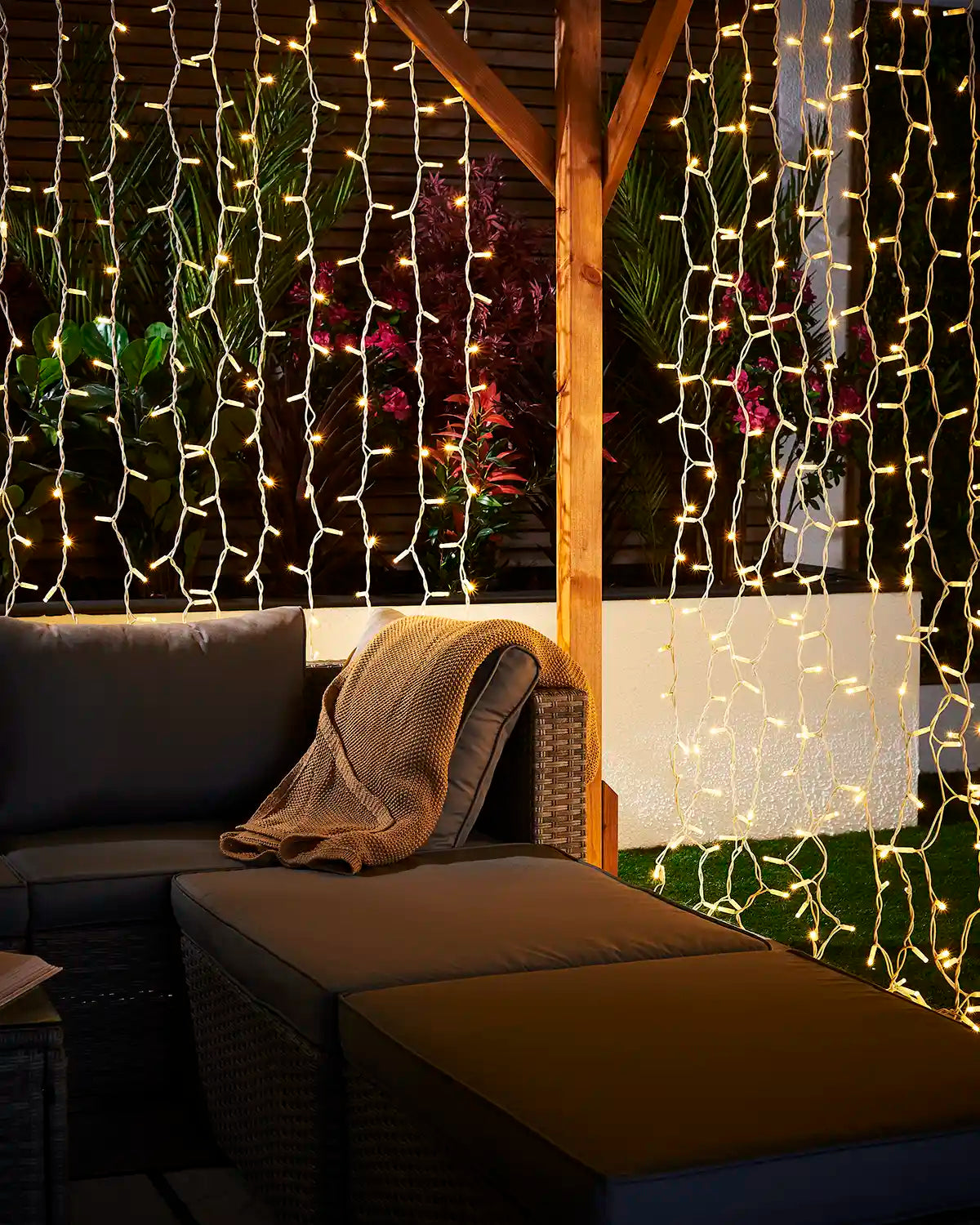 Warm white curtain lights on white cable displayed around a covered patio with outdoor seating.
