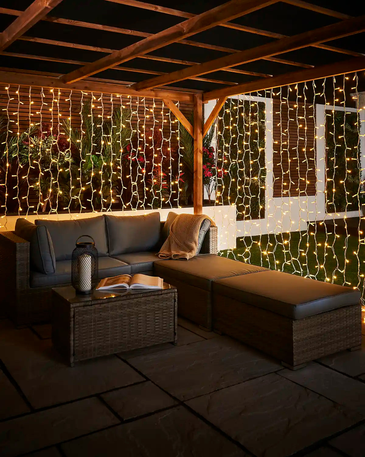 Warm white Pro Series curtain lights on white cable creating a glowing backdrop around garden seating.