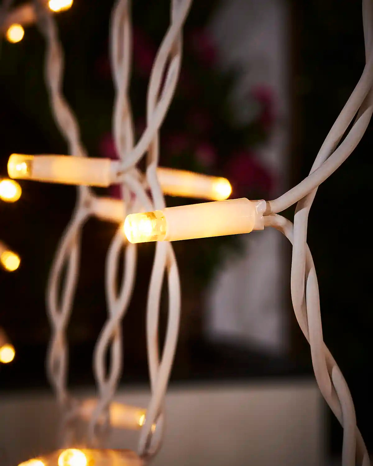 Close-up of warm white curtain light LEDs on white cable with hanging strands in the background.
