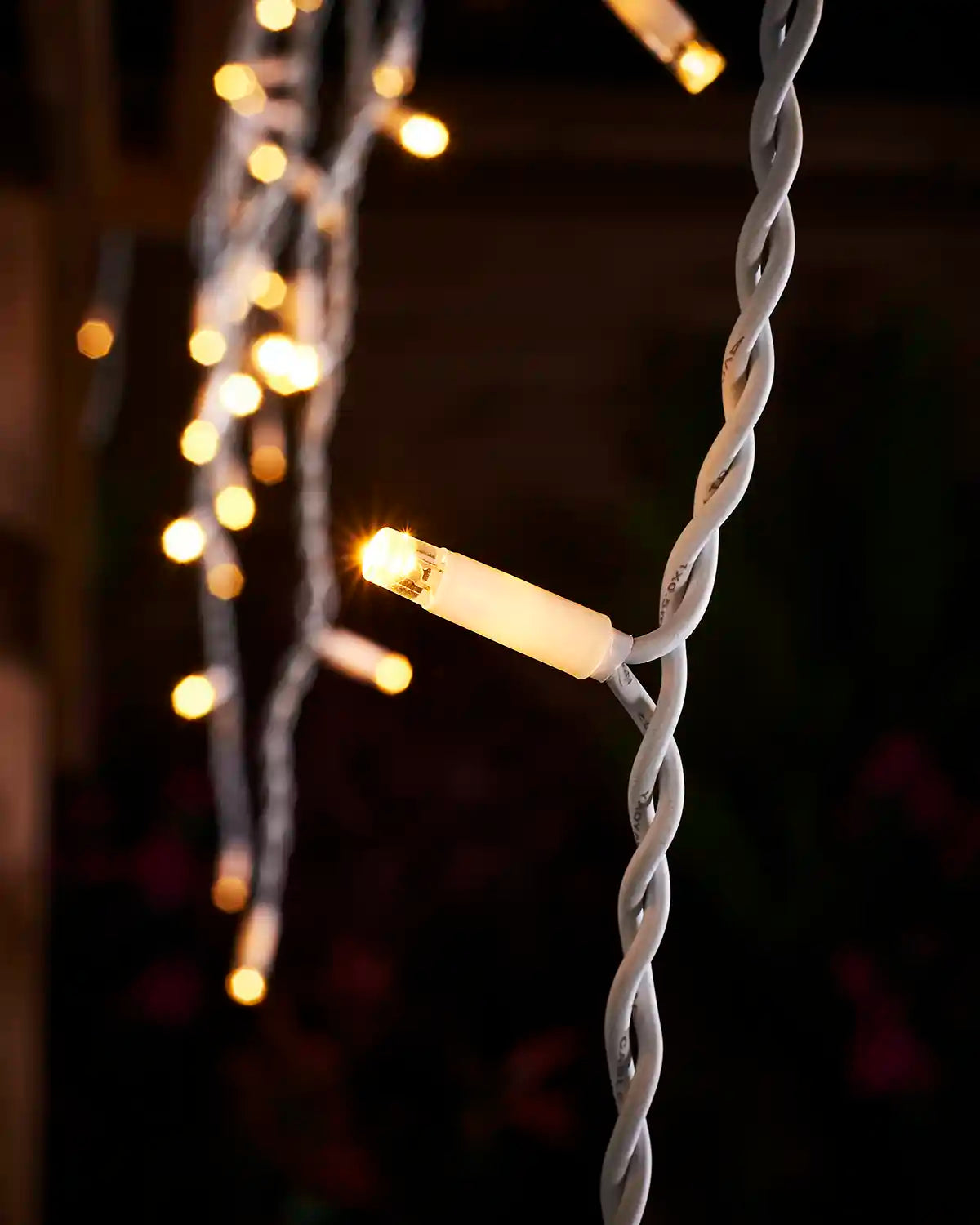 Close-up of a warm white LED icicle light on white twisted cable.