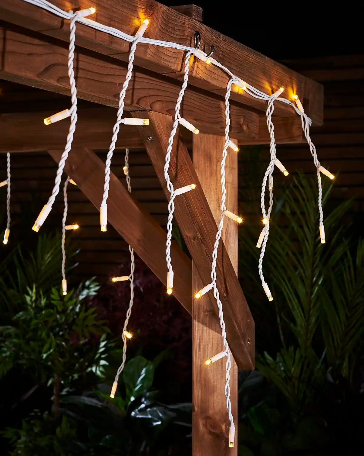 Warm white icicle lights hanging from a wooden pergola on white cable.