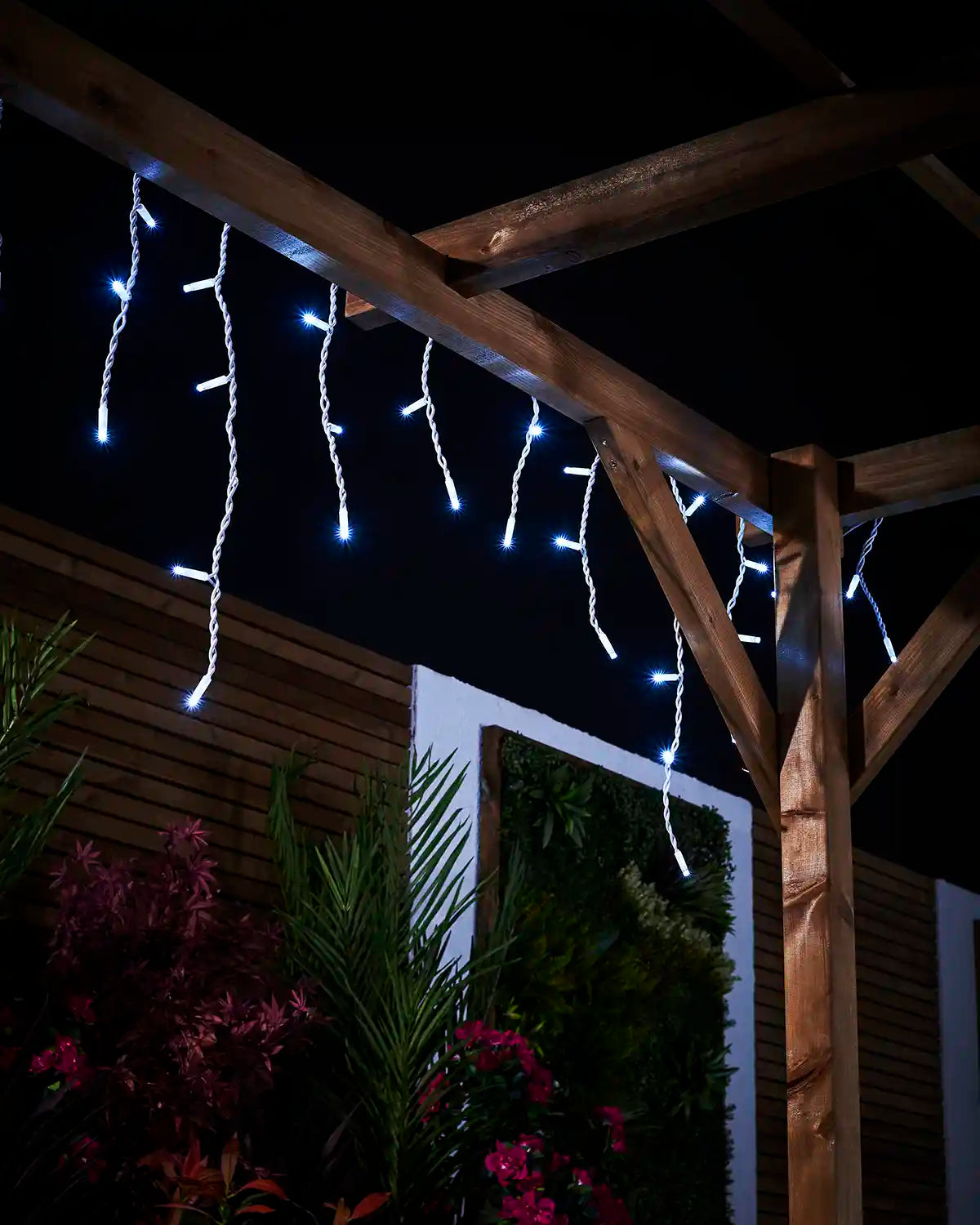 White icicle lights hanging from a wooden pergola with varied drops.