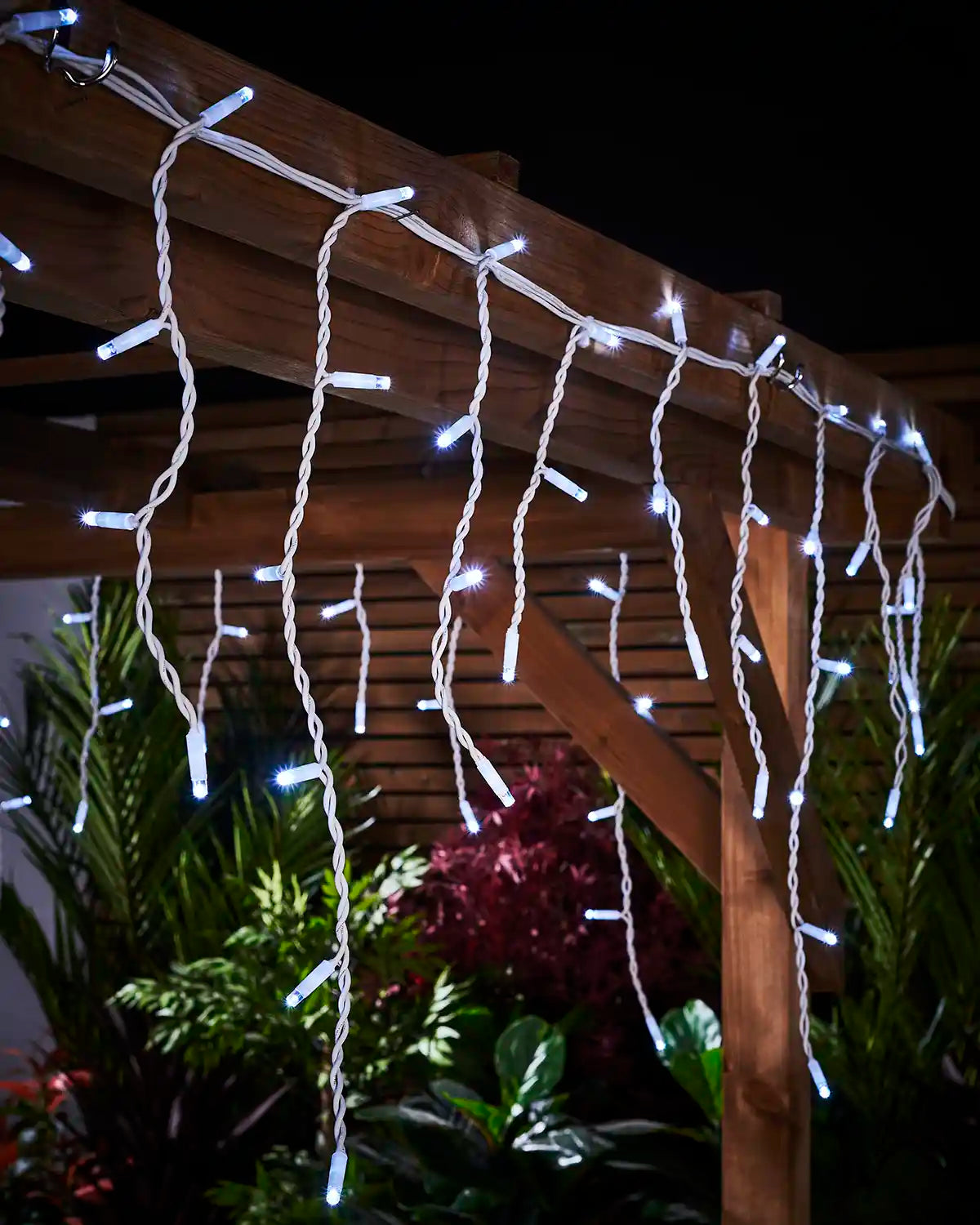 White icicle lights hanging from a wooden pergola on white cable.