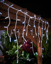 White icicle lights hanging from a wooden pergola on white cable.