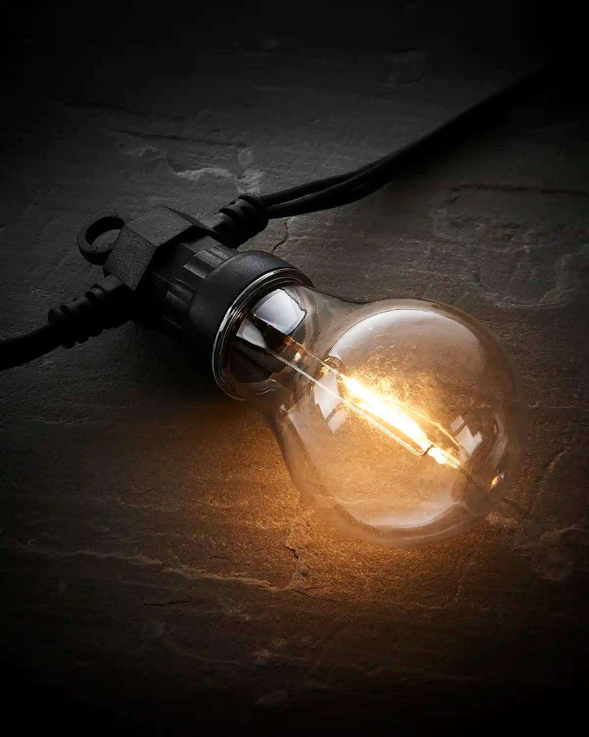Close-up of a warm white A60 filament festoon bulb on a black cable.