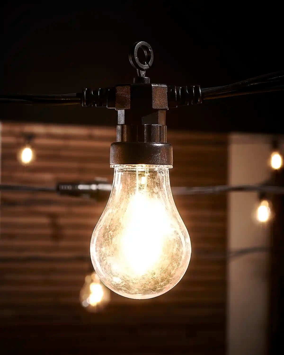 Close-up of a lit warm white A60 filament bulb with black Pro Series cable.