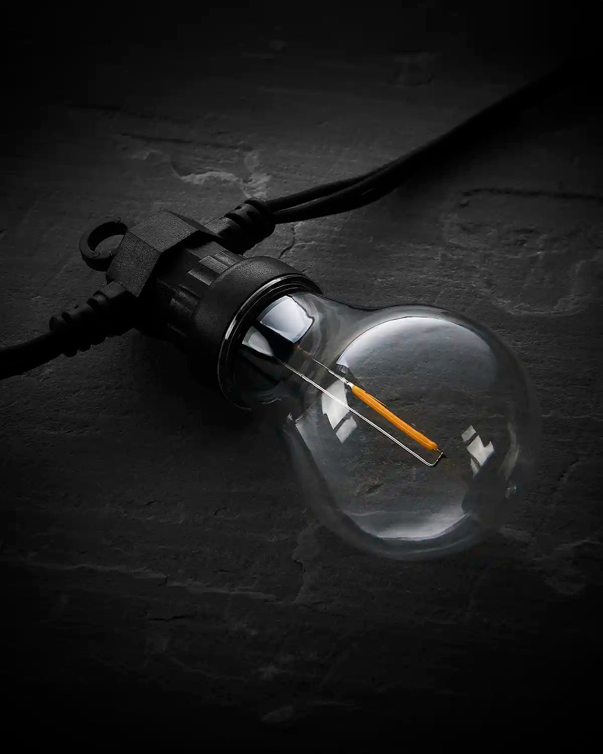 Unlit A60 filament festoon bulb on a black cable against a dark background.
