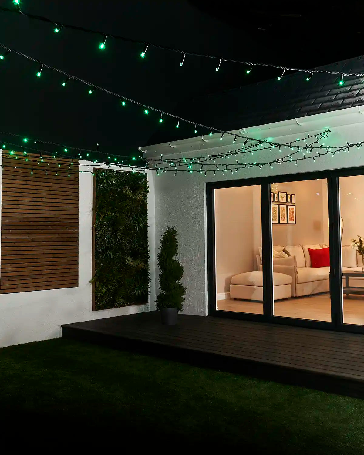 Green LED string lights suspended across an outdoor garden seating area.