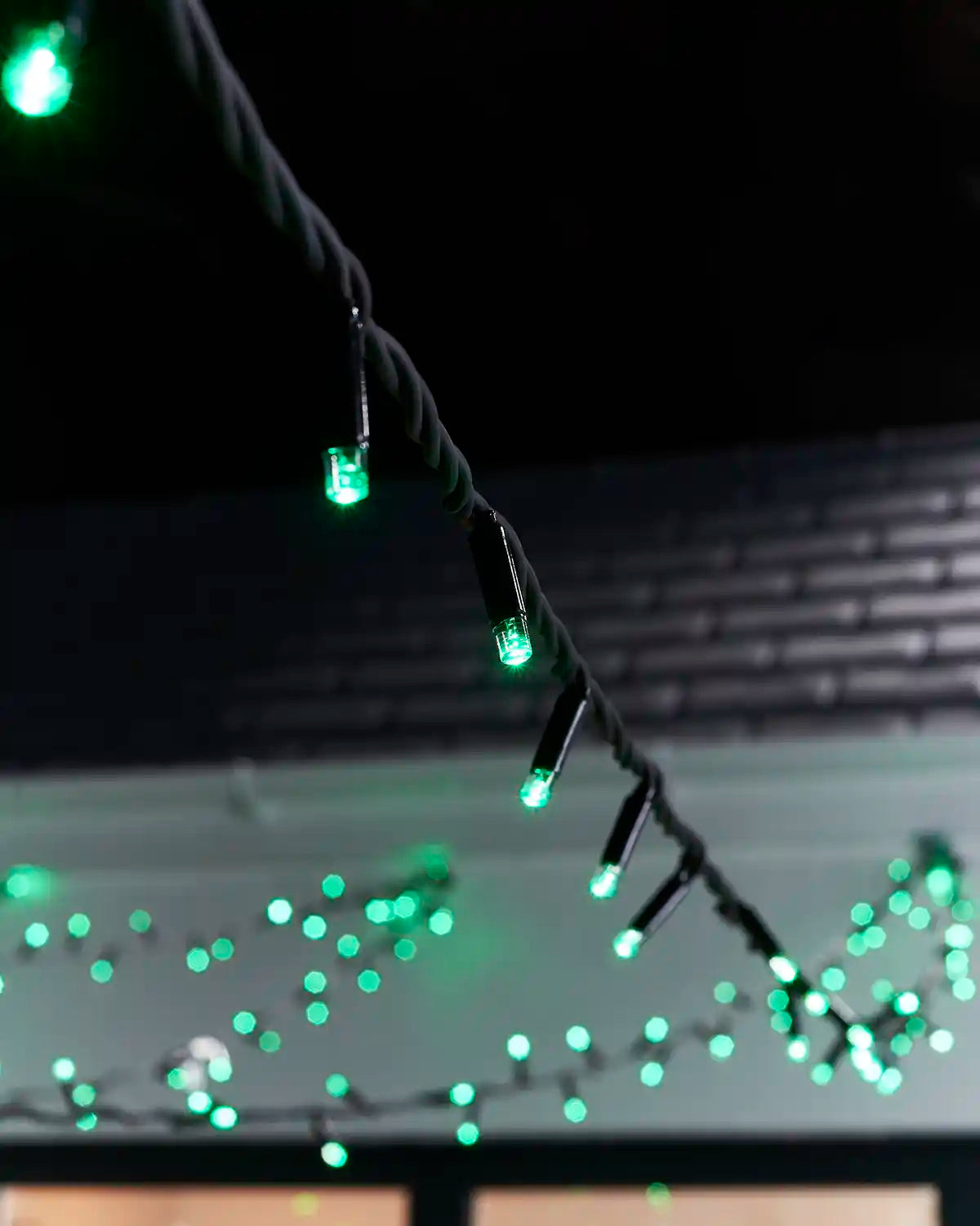 Close-up of green LED string lights on dark twisted cable.