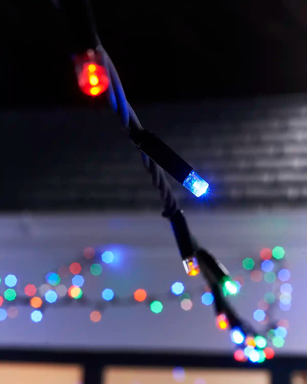Close-up of red, blue and green LED string lights on a black cable with blurred lights behind.