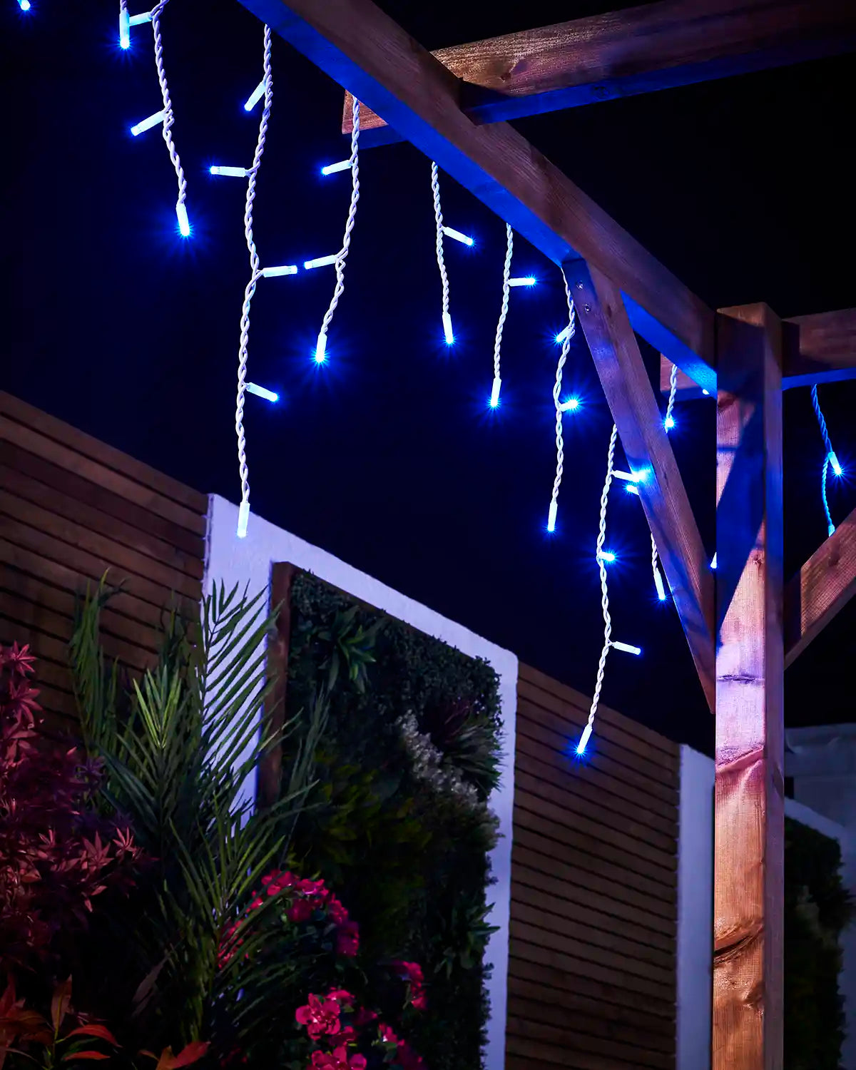 Blue icicle lights hanging from a pergola with white cable and varied drops.