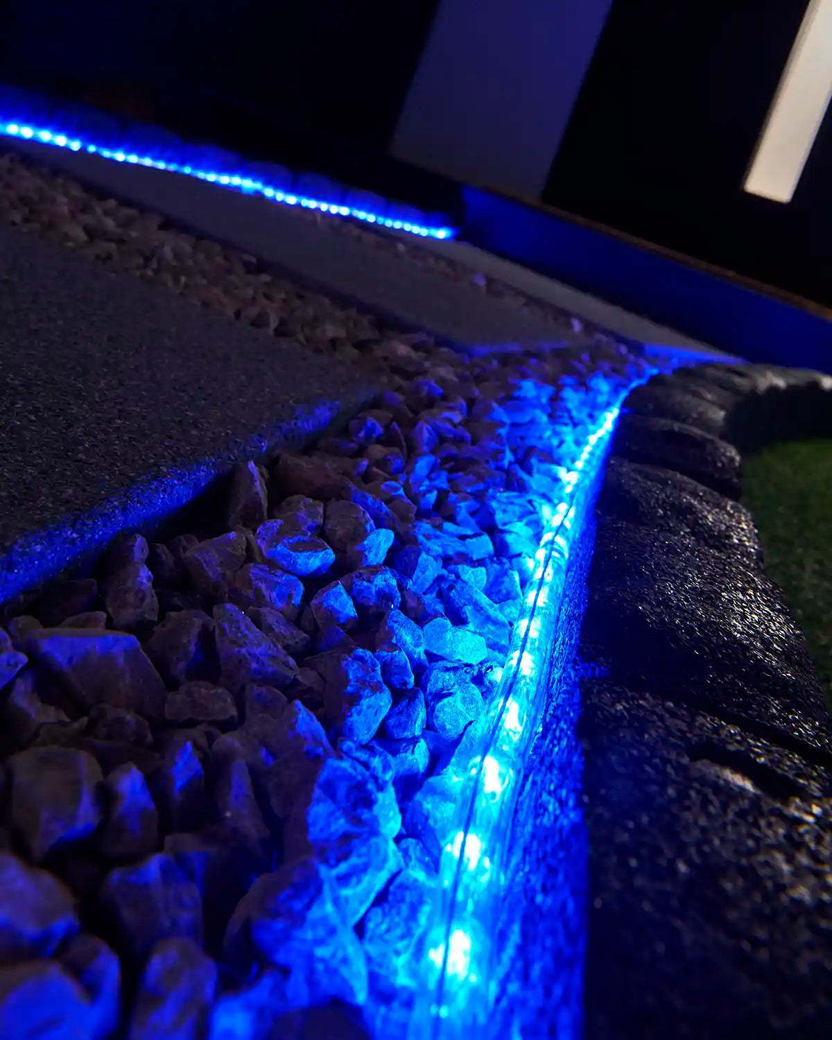 Blue rope light illuminating a stone border beside outdoor paving and gravel.
