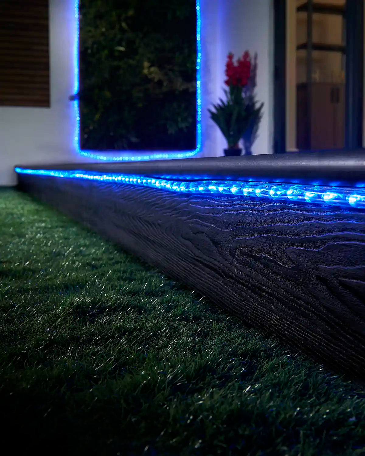 Blue rope light running along a garden step with a matching lit feature in the background.