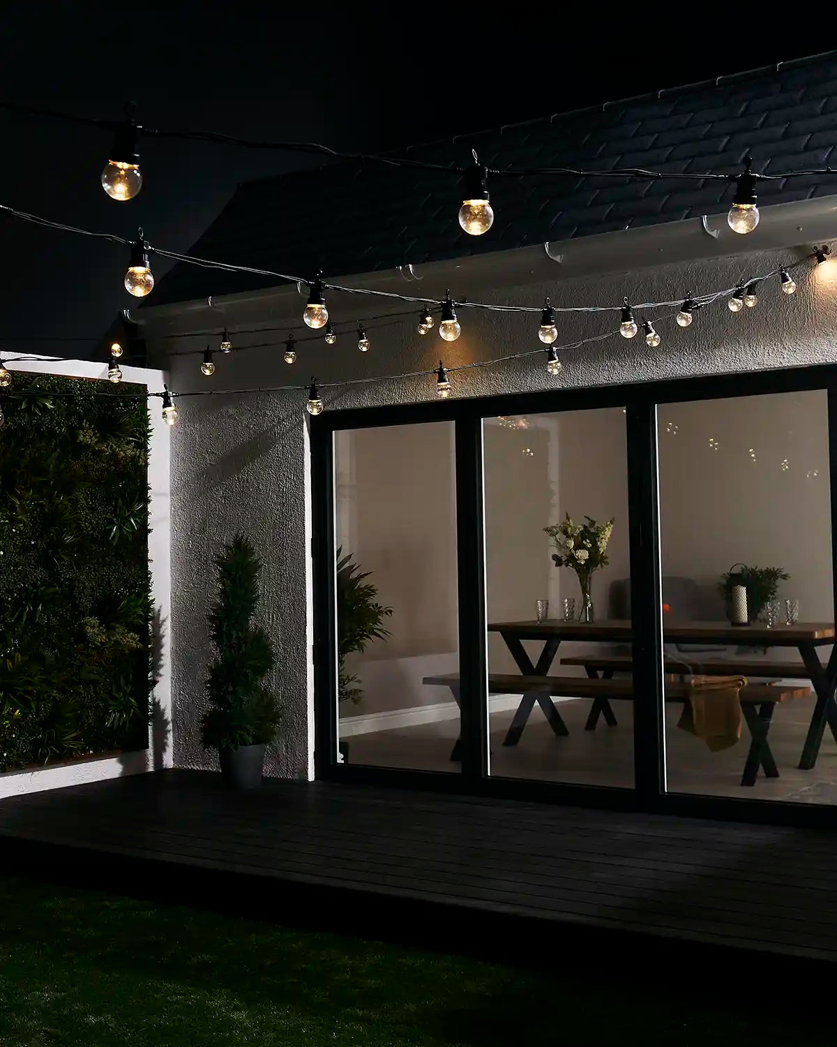 Warm white clear bulb festoon lights displayed above a garden patio and house exterior.