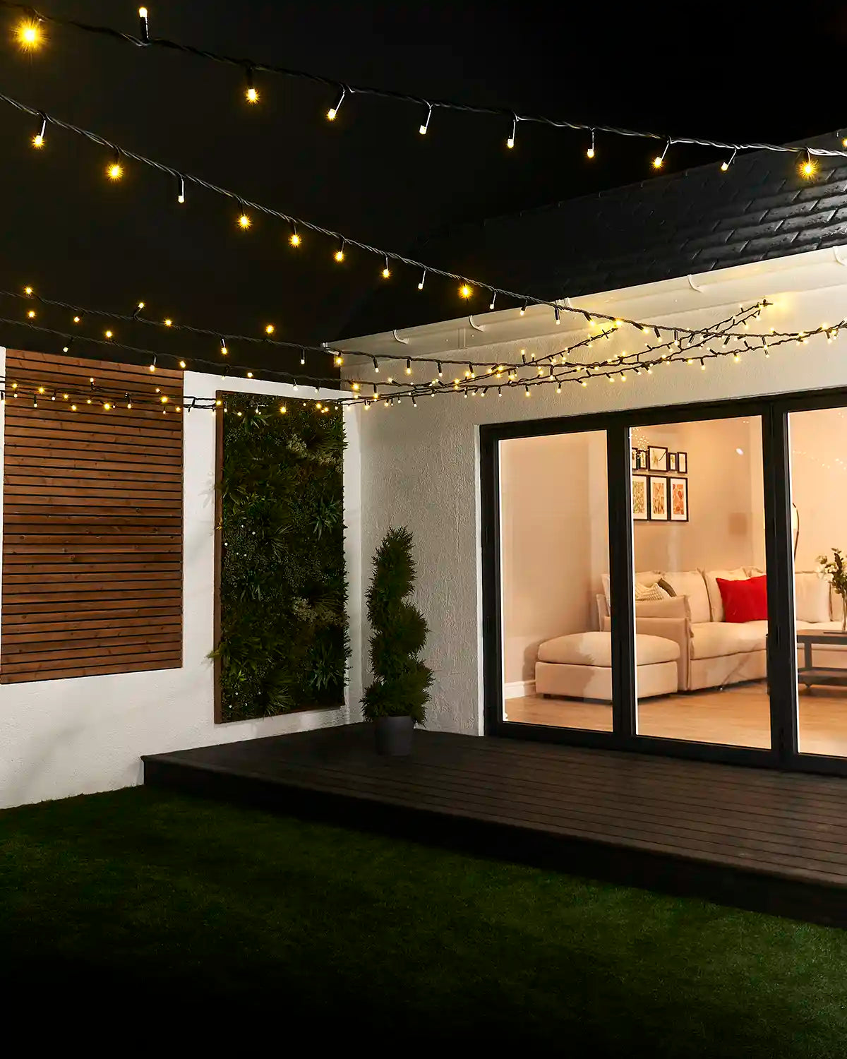 Gold string lights with black cable suspended overhead across a garden seating area.