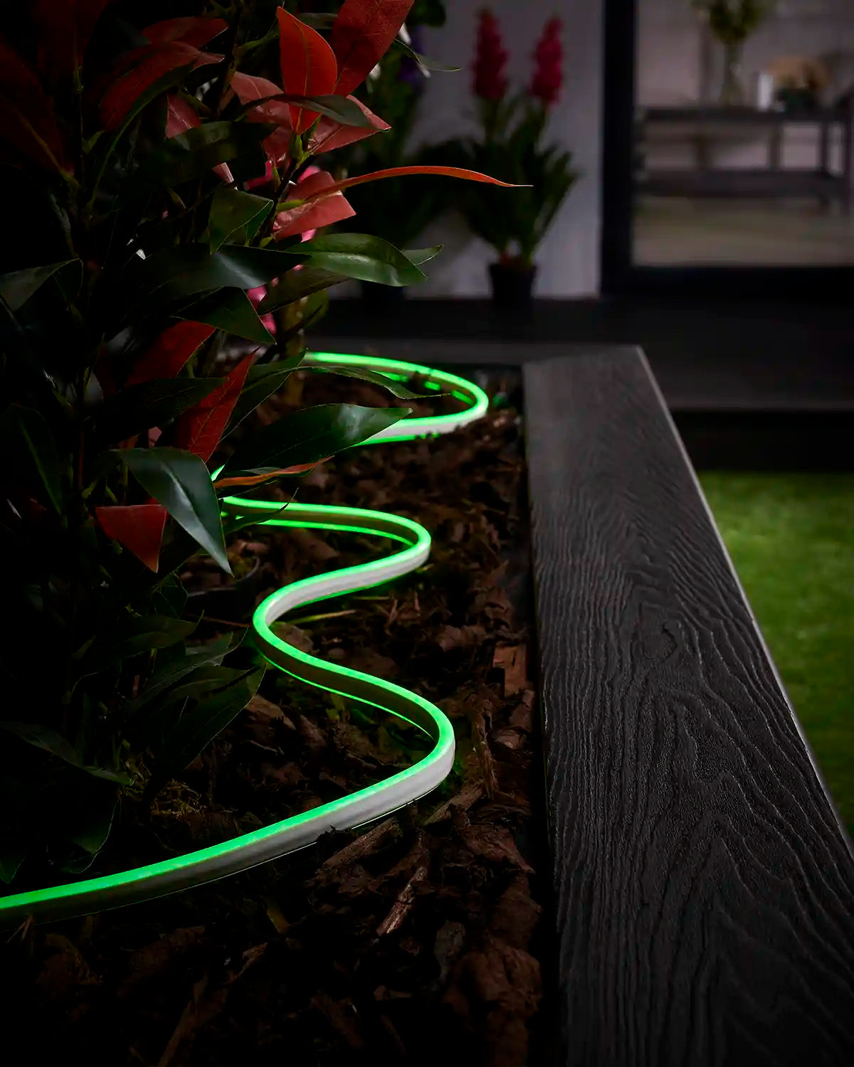 Green neon flex lighting laid through bark around plants beside a raised garden border.