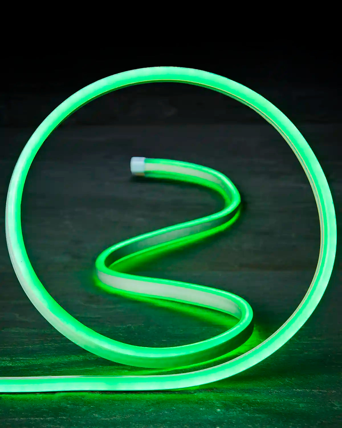 Close-up of green neon flex shaped into a loop on a dark surface.