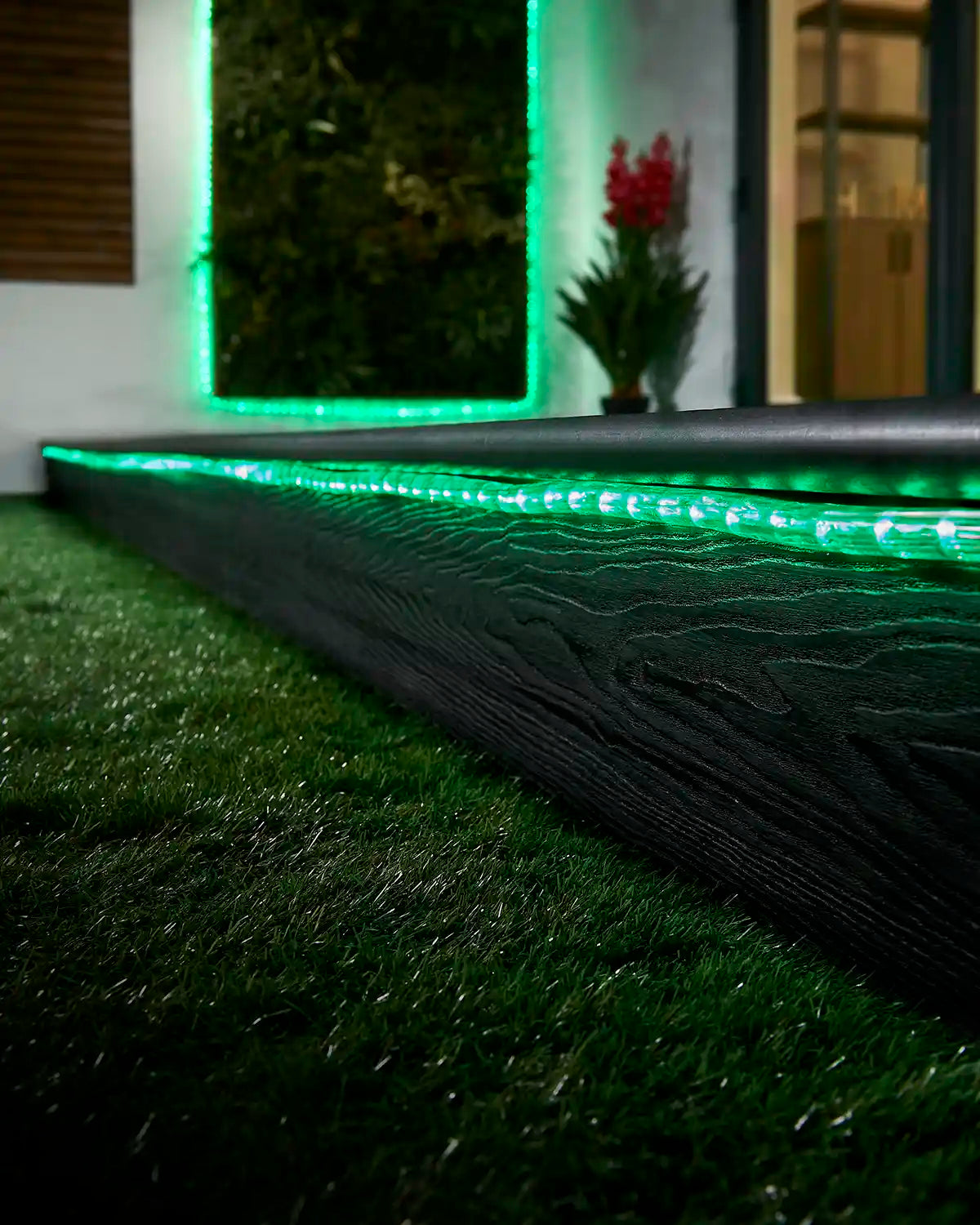 Green rope light running along a garden step with a matching lit feature in the background.