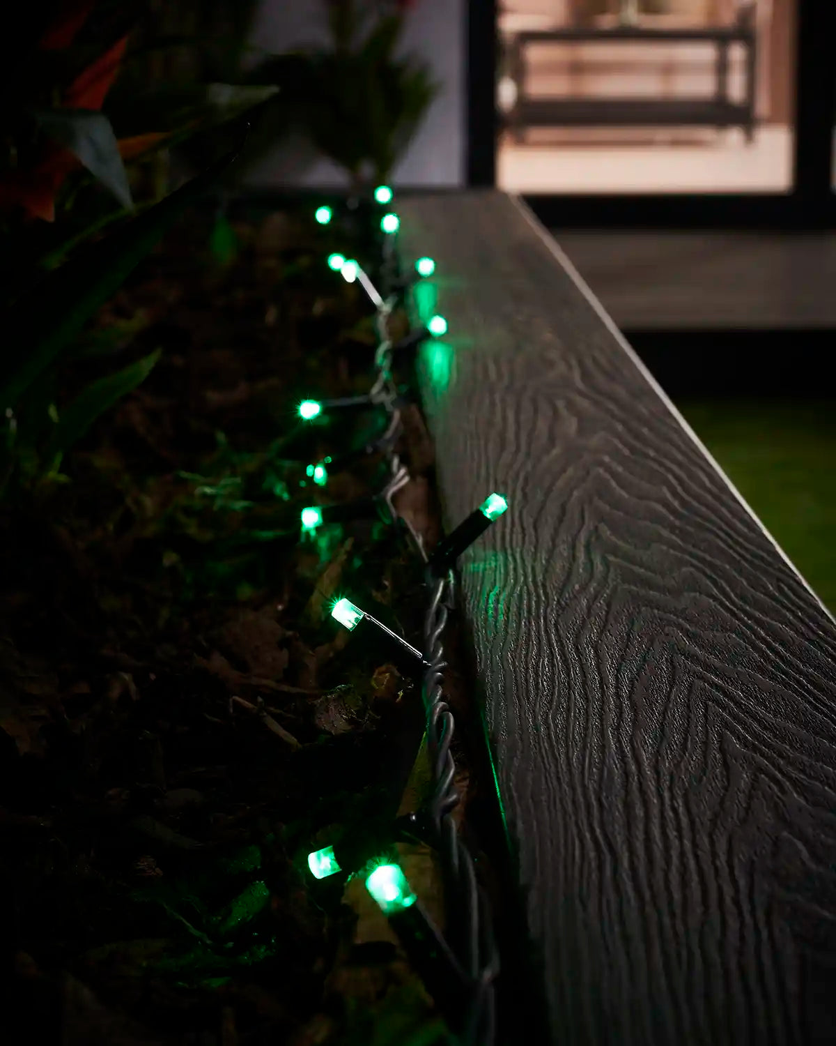 Green LED string lights displayed along the edge of an outdoor planter.