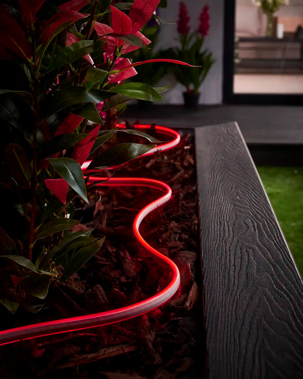 Red Neon Flex lighting curved through bark around plants in a garden planter.