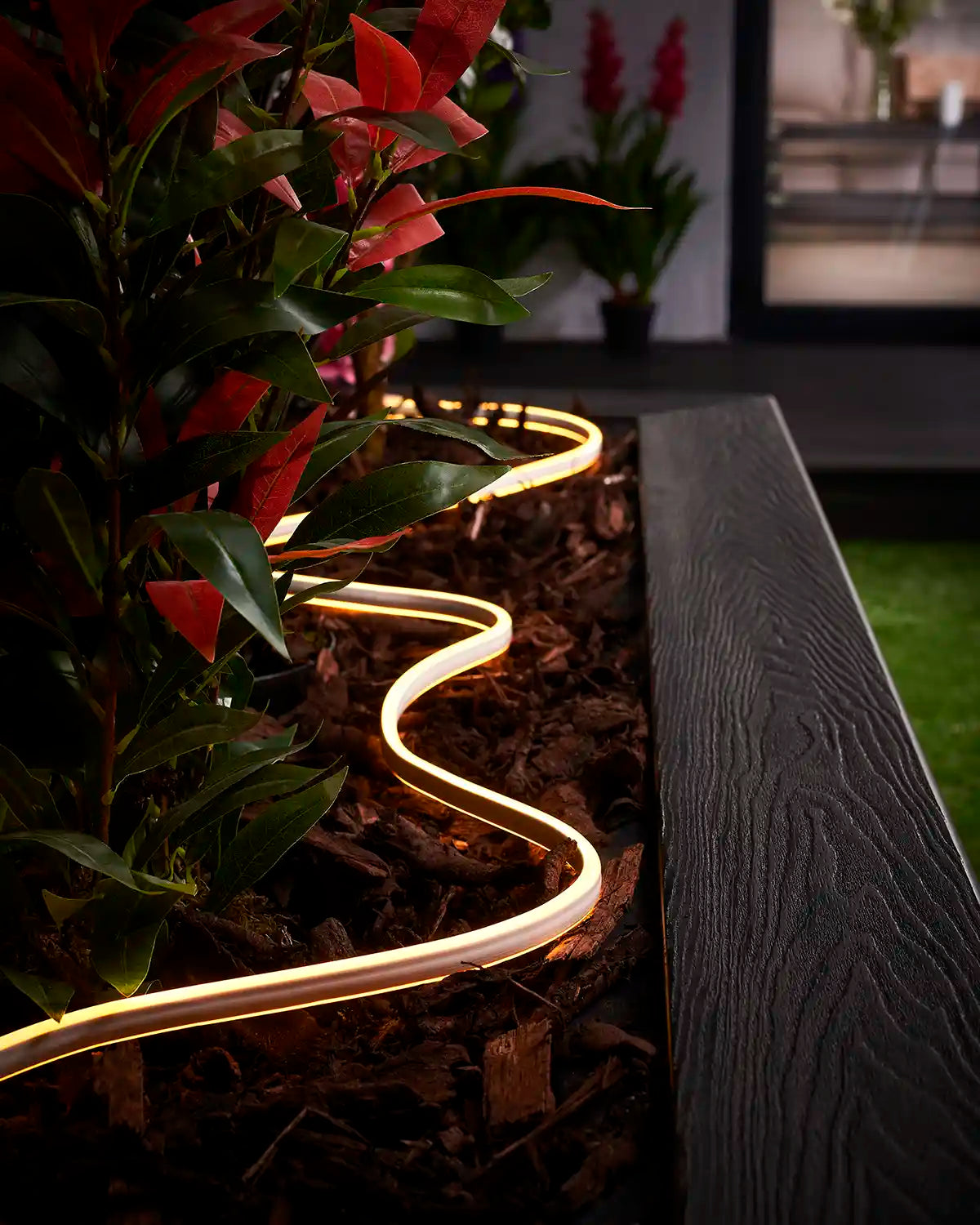 Warm white Neon Flex lighting curved through bark around plants in a garden planter.