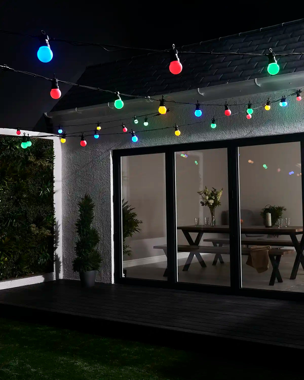 Multi colour festoon lights displayed above a garden patio and house exterior.