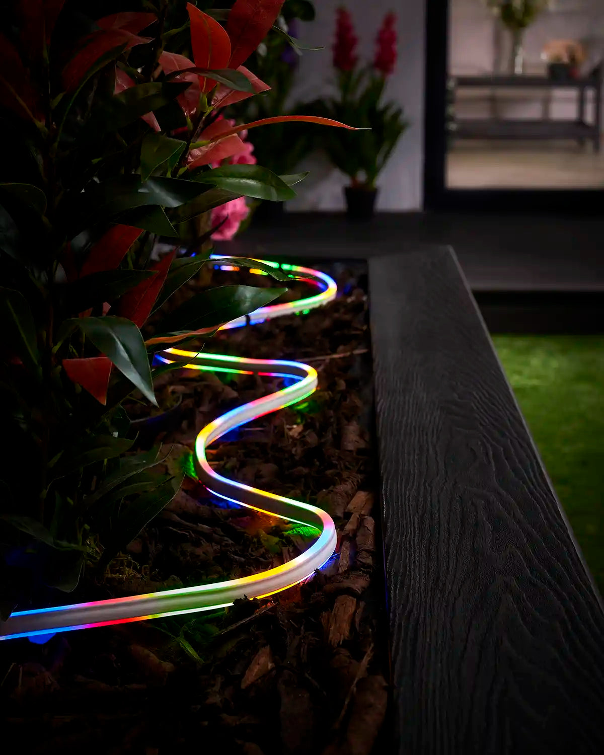 Multi colour neon flex lighting laid through bark around plants beside a raised garden border.