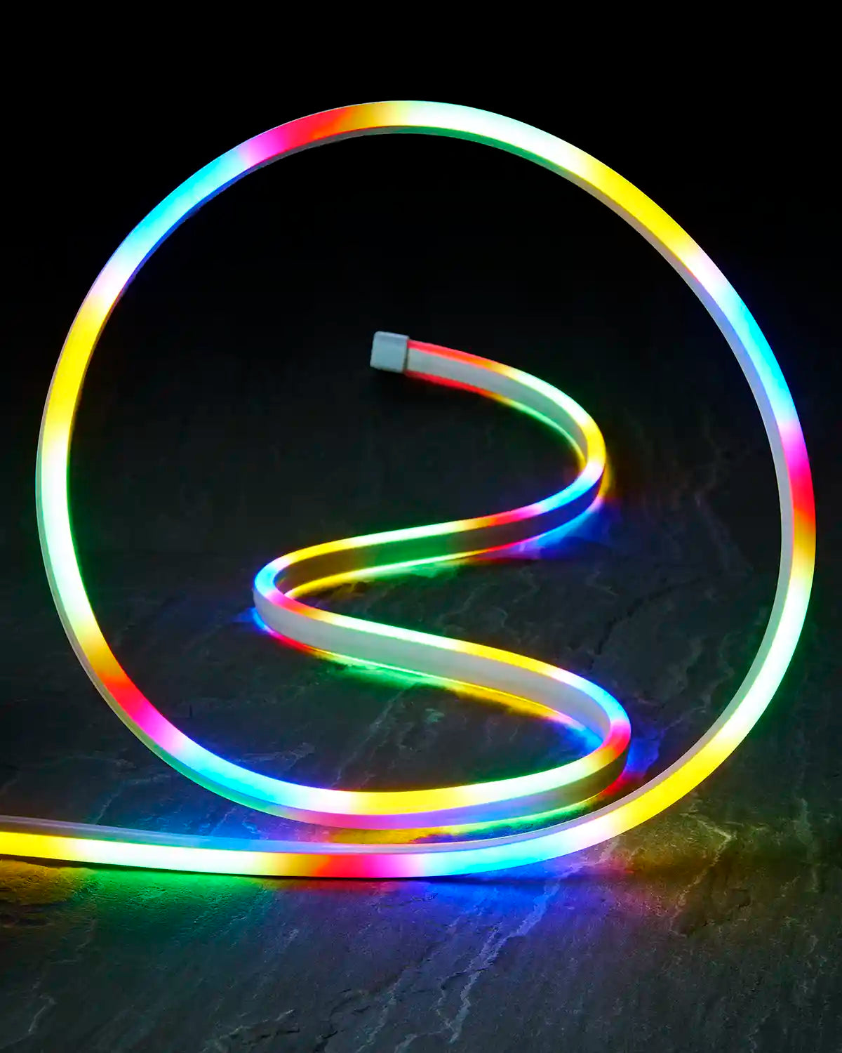 Close-up of multi colour neon flex shaped into a loop on a dark surface.