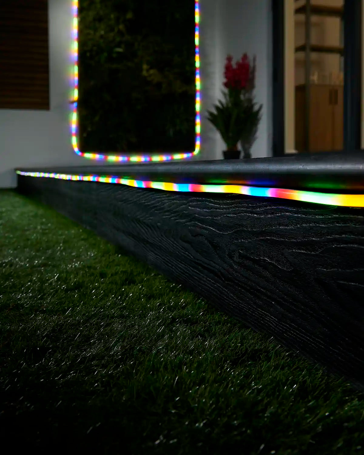 Multi colour neon flex lighting along a garden step with a matching lit feature in the background.