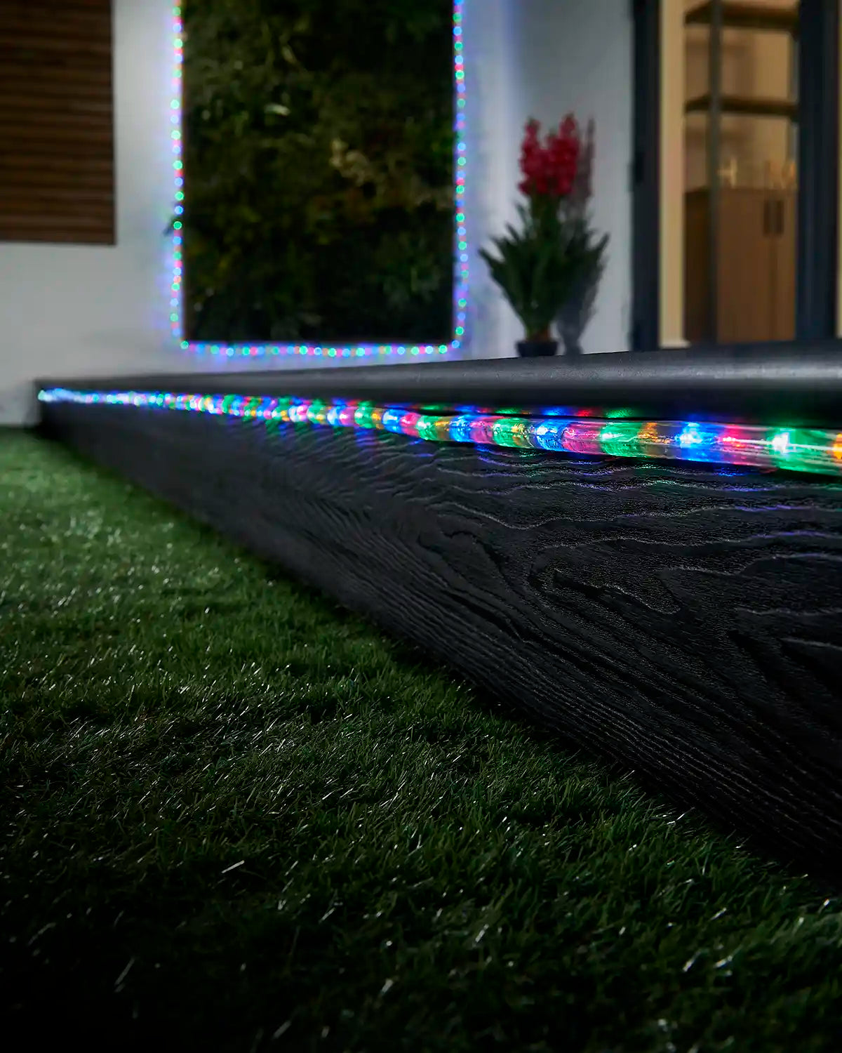 Multi colour rope light running along a garden step with a matching lit feature in the background.