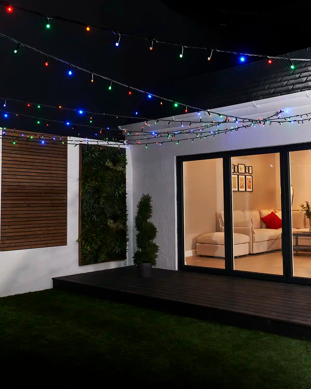 Multi colour string lights hung across an outdoor garden patio at night.