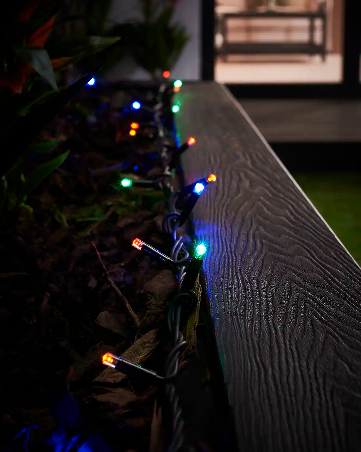 Multi colour LED string lights arranged along the edge of an outdoor planter at night.