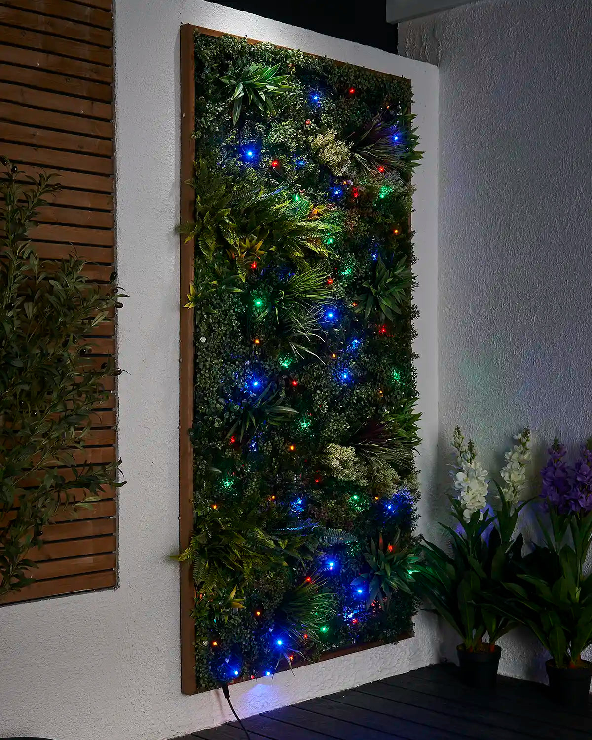 Multi colour LED string lights displayed across a green wall panel in an outdoor seating area.