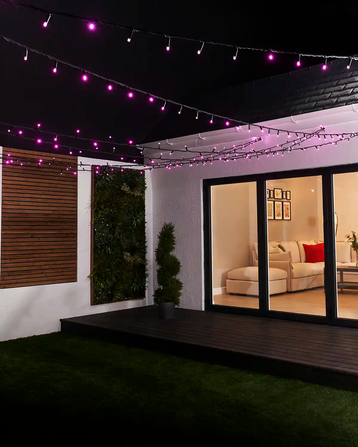 Pink string lights with black cable suspended overhead across a garden seating area.