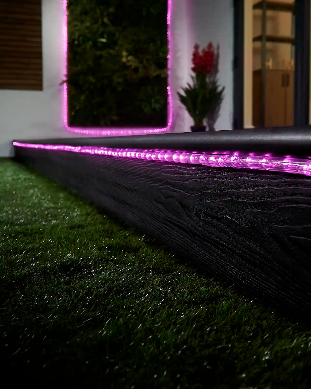 Pink rope light running along a garden step with a matching lit feature in the background.