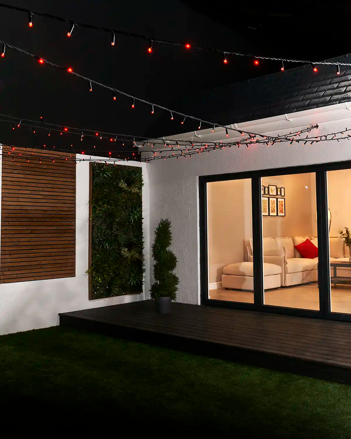 Red string lights with black cable suspended overhead across a garden seating area.