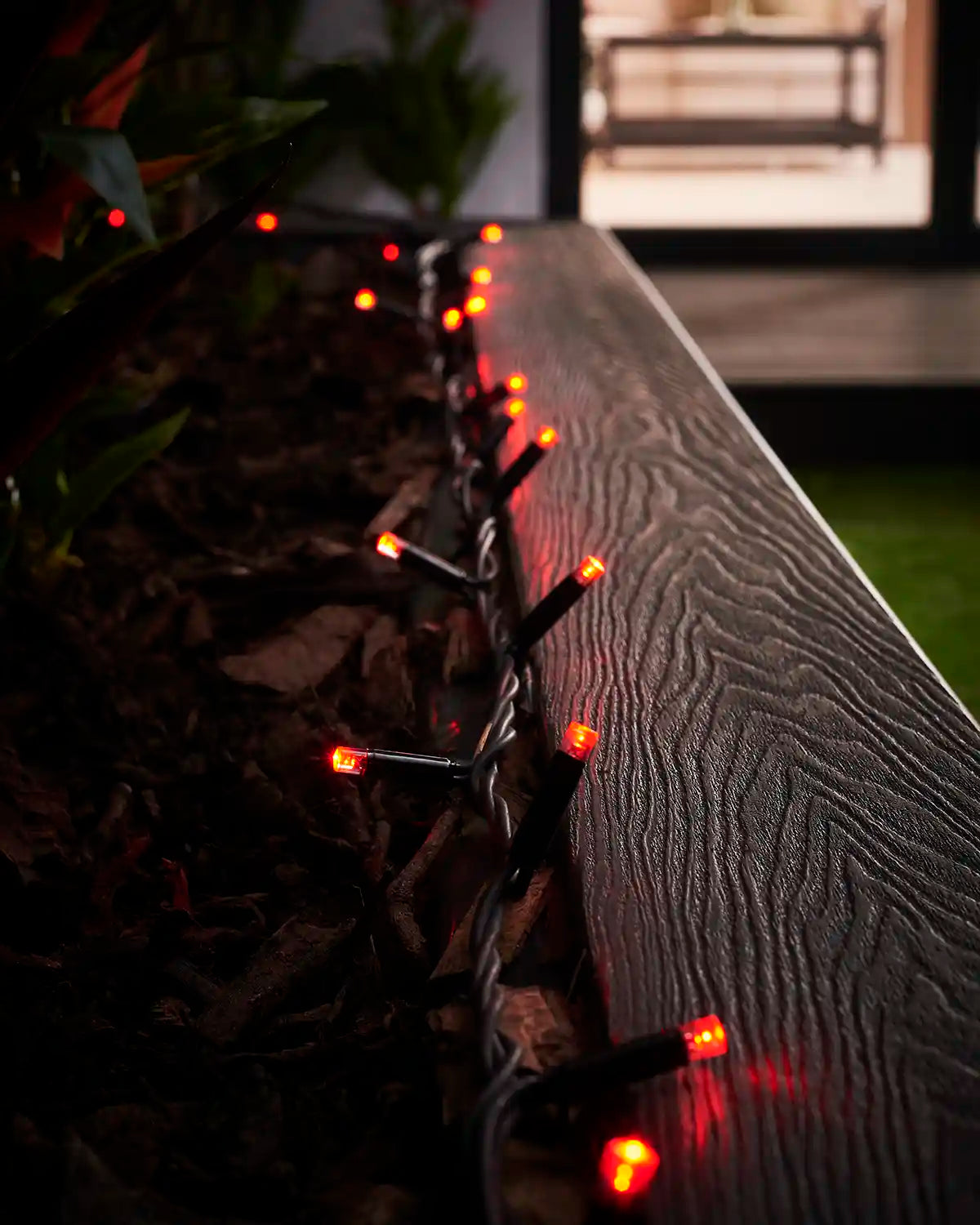 Red LED string lights on black cable running along an outdoor planter rail.