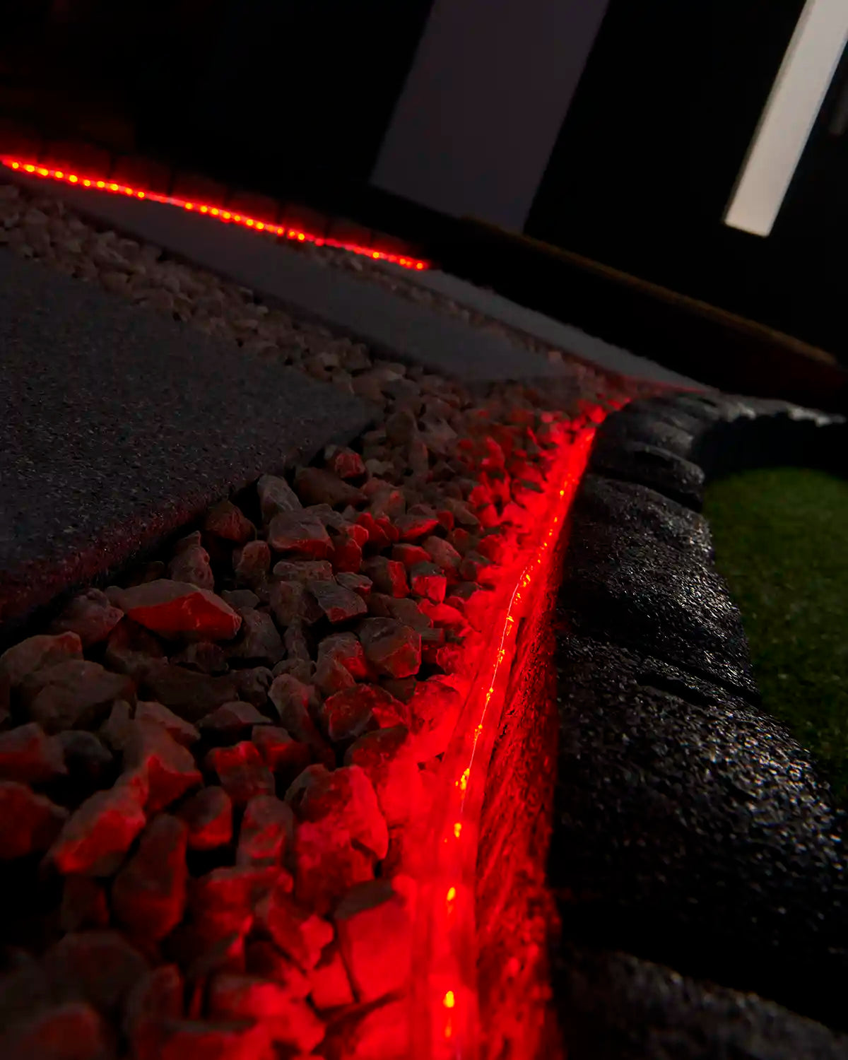 Red rope light illuminating a stone border beside outdoor paving and gravel.