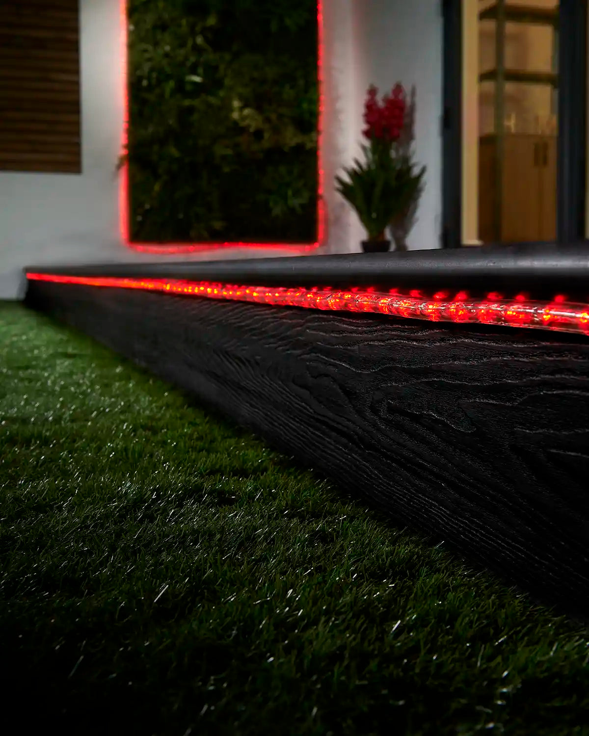 Red rope light running along a garden step with a matching lit feature in the background.